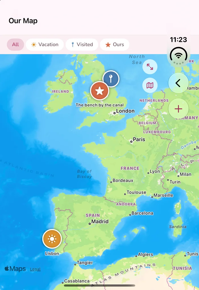 Love You Bye on the iPhone Duo's
               folded cover screen. A map of western Europe fills the full width of the display,
               with pins on England for &lsquo;The bench by the canal&rsquo; and a sun marker near
               Lisbon. Along the top, a header reading &lsquo;Our Map&rsquo; and filter buttons for
               All, Vacation, Visited and Ours. The clock reading 11:23 and a wifi icon sit in a
               vertical strip down the right-hand edge, directly on top of the app's back arrow
               and its plus button.